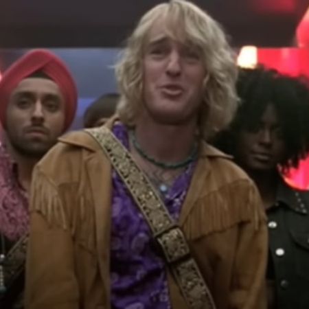 Owen Wilson is wearing a brown cowboy jacket as few people are standing behind him.